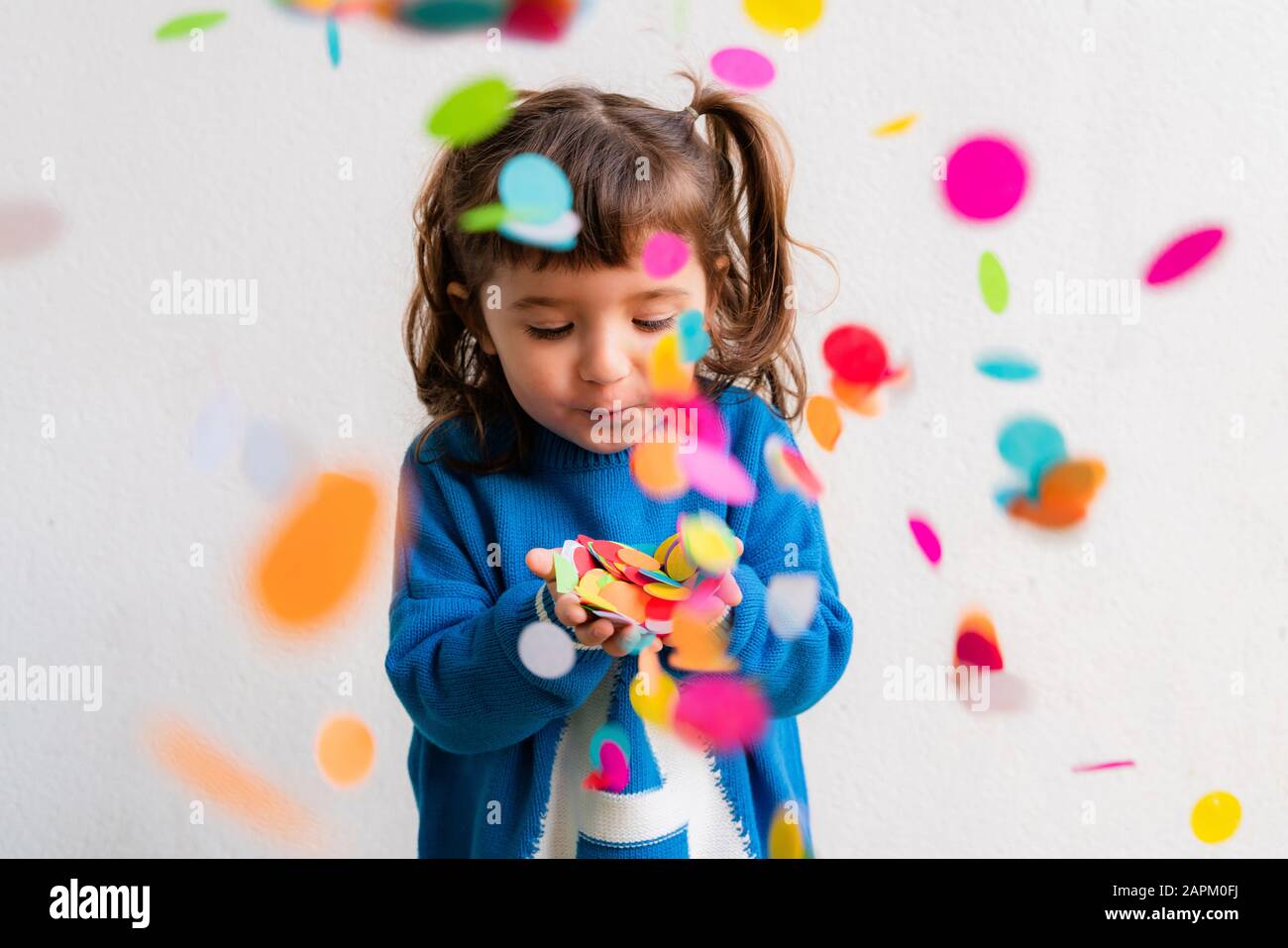 Fröhliches kleines Mädchen, das die Konfetti auf einer Party vor einer weißen Wand weht Stockfoto
