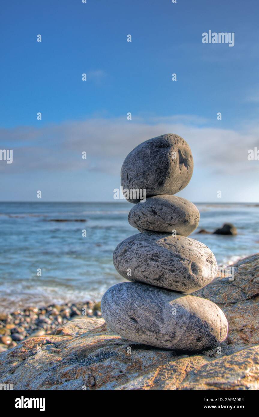 Selektive Fokusaufnahme von gestapelten Steinen in einer Meeresküste mit Ein verschwommener blauer Himmel im Hintergrund Stockfoto