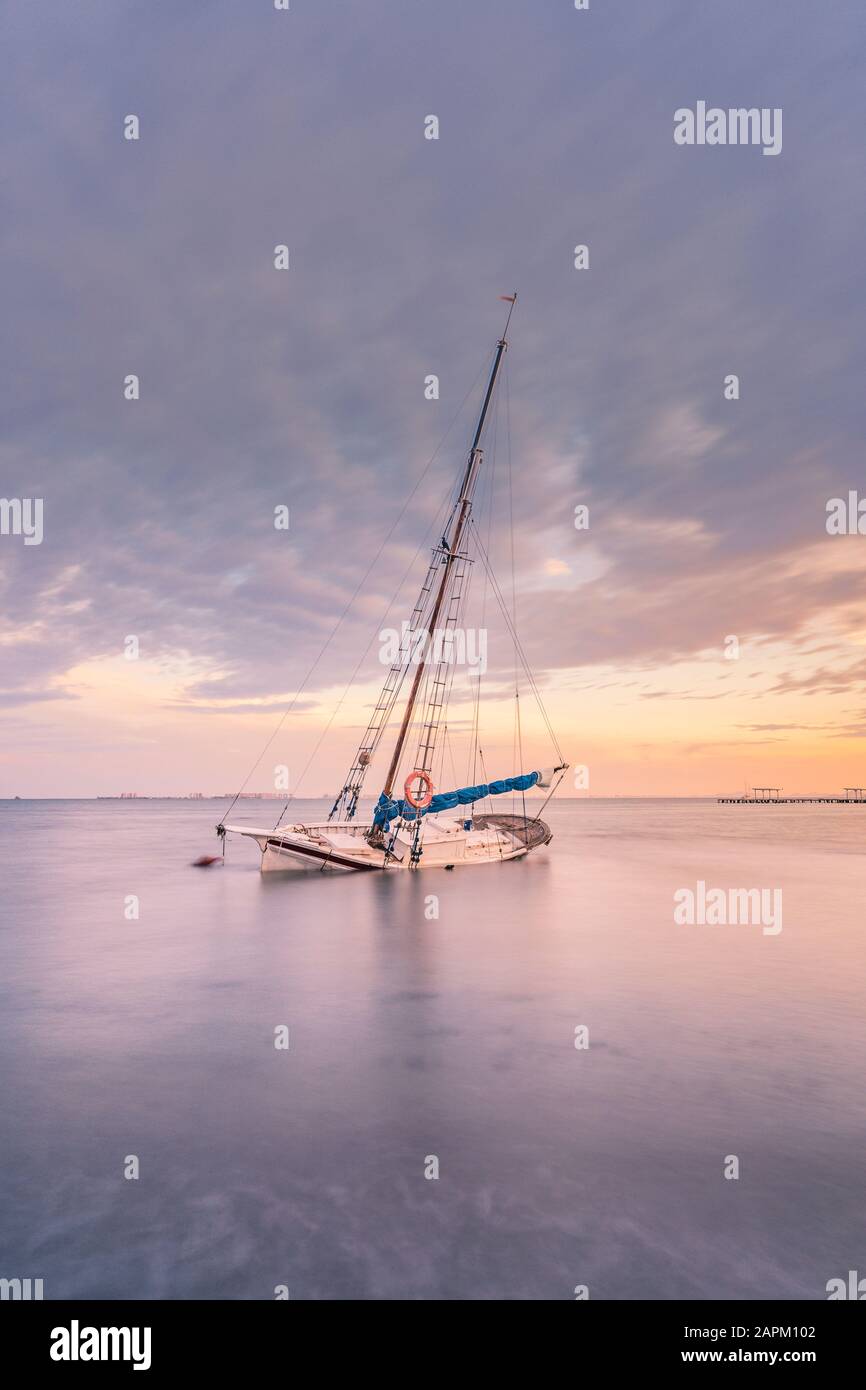 Spanien, Murcia, Santiago de la Ribera, verlassenes Segelboot auf ruhigem Meer bei Sonnenuntergang Stockfoto