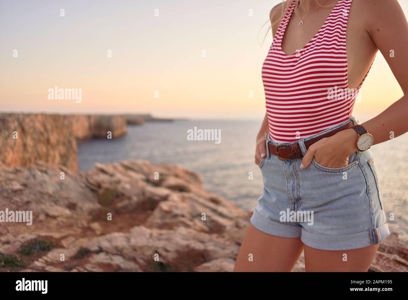 Junge Frau, die Sonnenuntergang am Meer genießt und auf einer Klippe steht Stockfoto