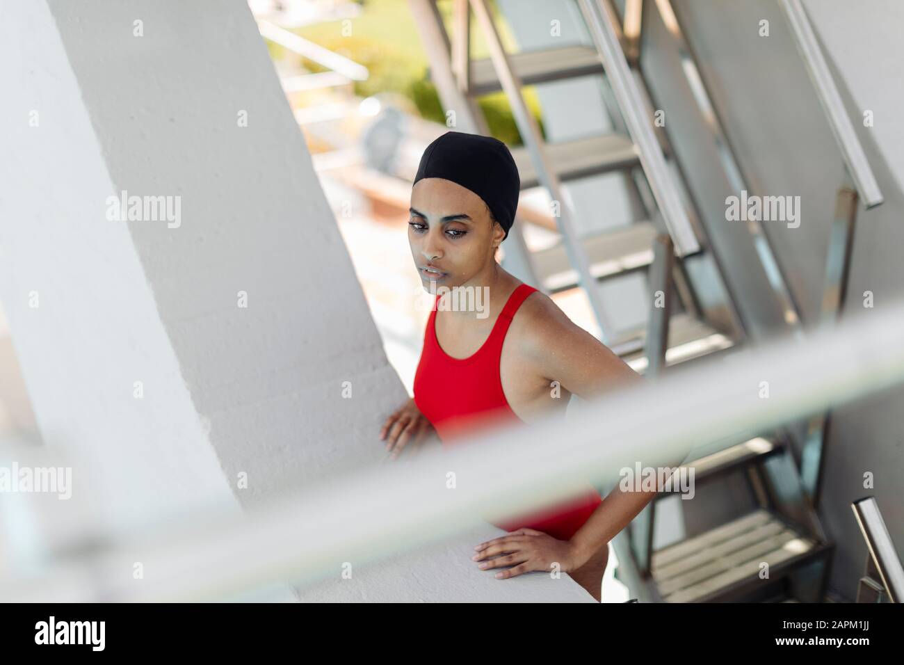 Porträt der jungen Frau mit Schwimmkappe und rotem Badeanzug, der auf einer Treppe auf dem Hochbrett steht Stockfoto