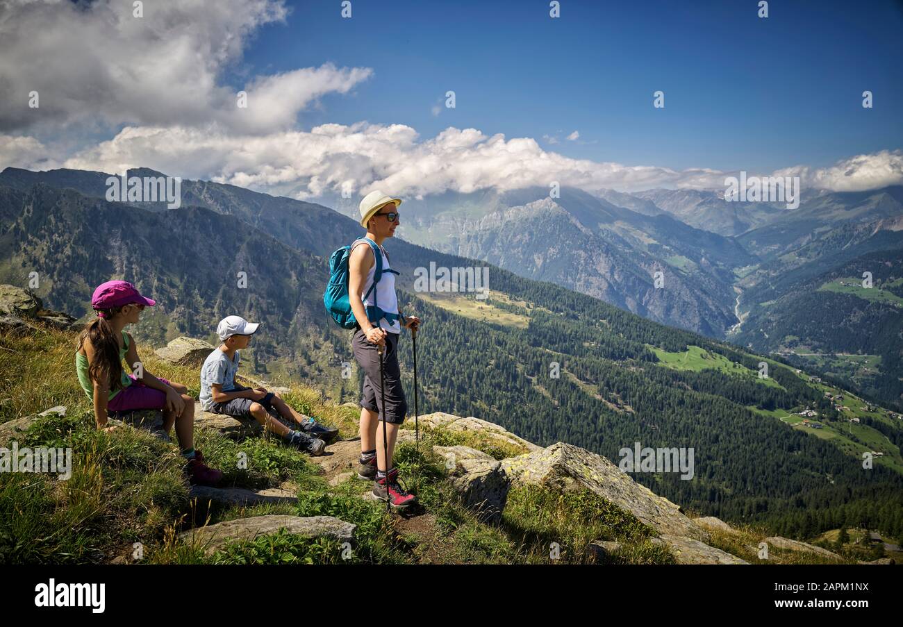 Mutter mit zwei Kindern, die eine Pause vom Wandern in der Alpenlandschaft, Passeiertal, Südtirol, Italien, einlegen Stockfoto