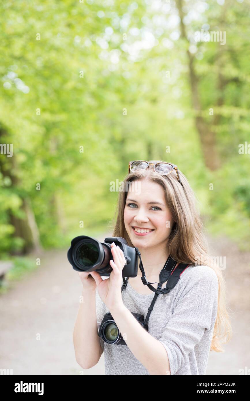 Porträt einer lächelnden jungen Frau, die zwei verschiedene Kameras im Freien vergleicht Stockfoto