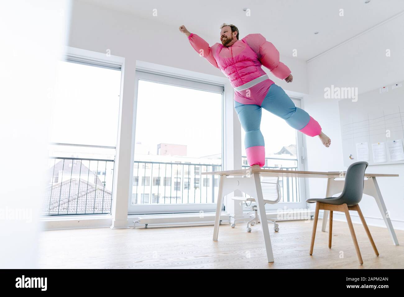 Geschäftsmann im Büro mit pinkfarbenem Bodybuilder-Kostüm, das vorgibt zu fliegen Stockfoto