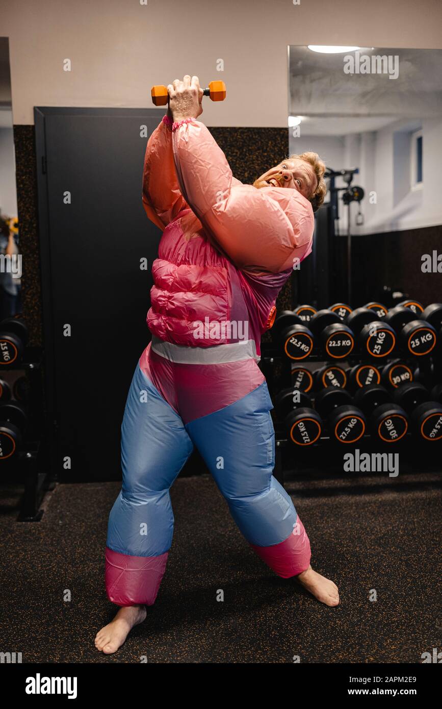 Mann im Fitnessstudio mit pinkfarbenem Body Builder Kostüm mit Hanteln Stockfoto