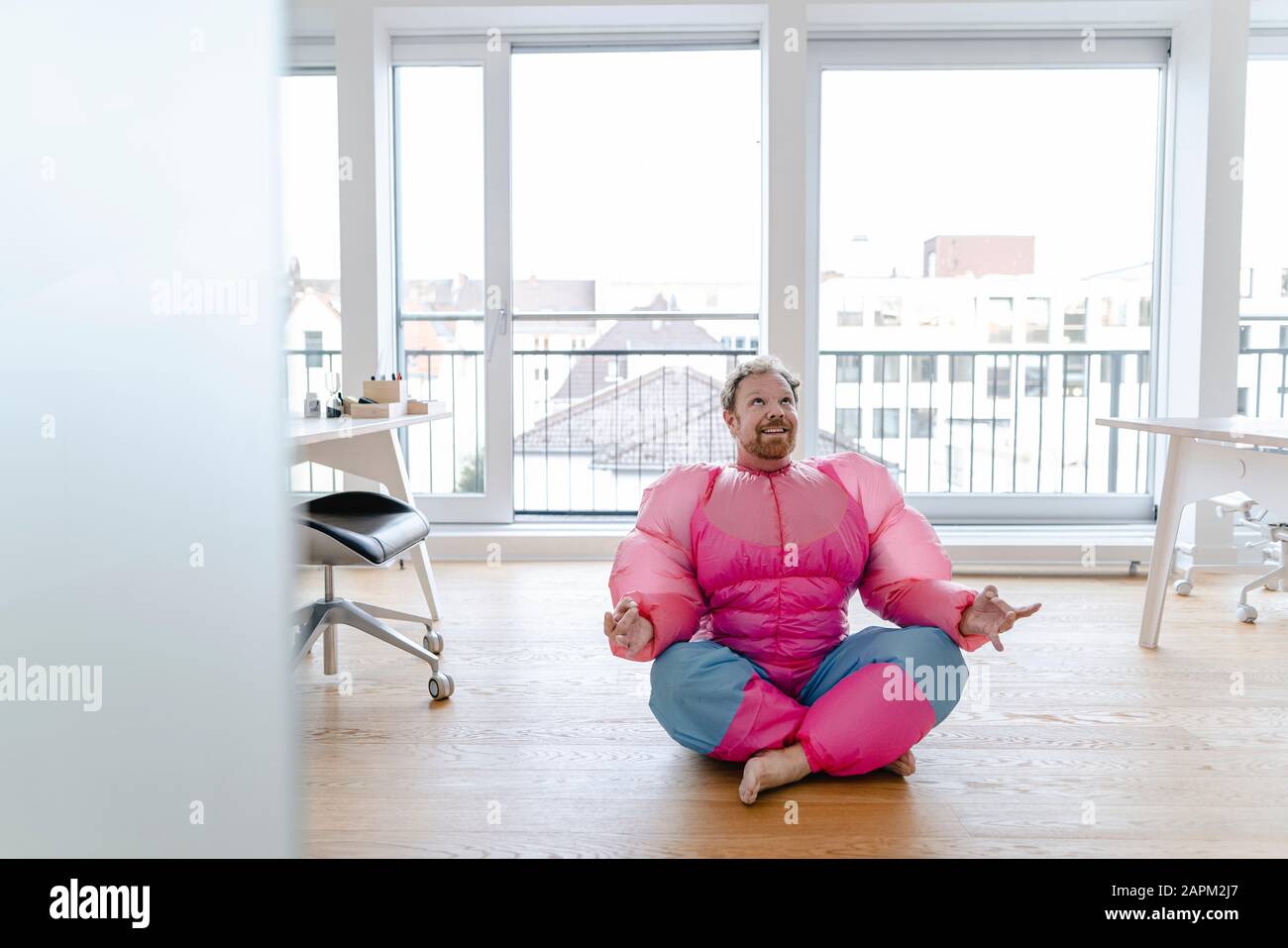 Geschäftsmann im Büro mit pinkfarbenem Bodybuilder-Kostüm, das Yoga praktiziert Stockfoto
