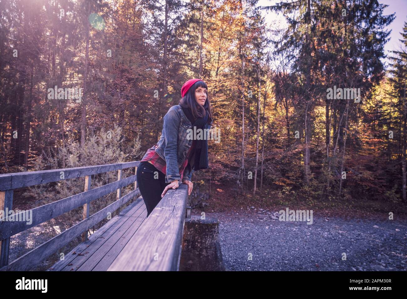 Frau trägt im Herbst roten wolligen Hut und Denimjacke auf einer Brücke Stockfoto