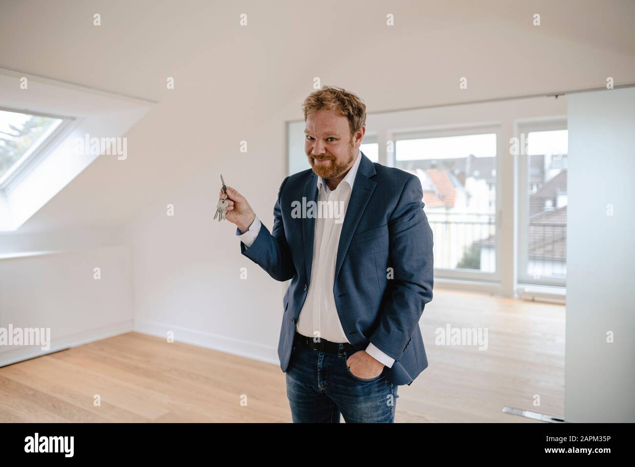 Portrait eines lächelnden Geschäftsmannes, der in einer leeren Wohnung mit Schlüssel steht Stockfoto