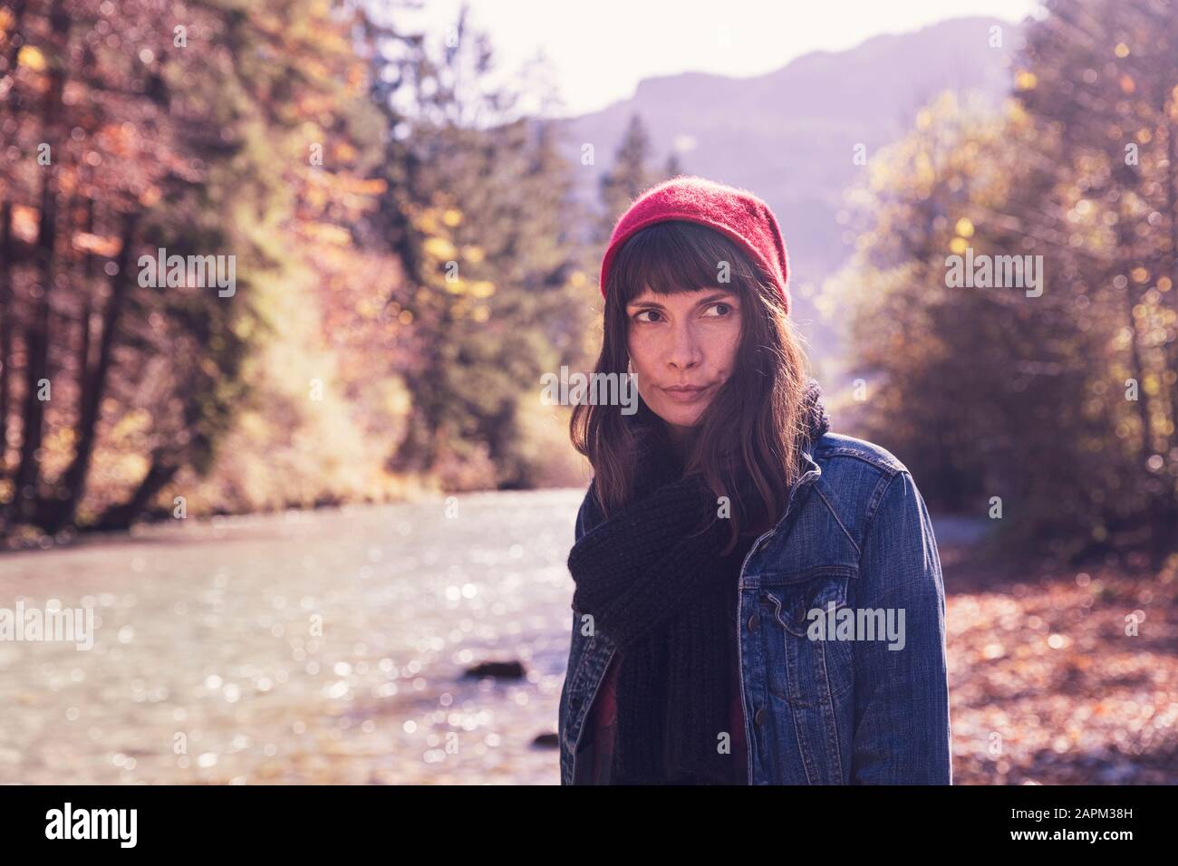 Frau mit rotem wolligem Hut und Denimjacke am Flussufer Stockfoto