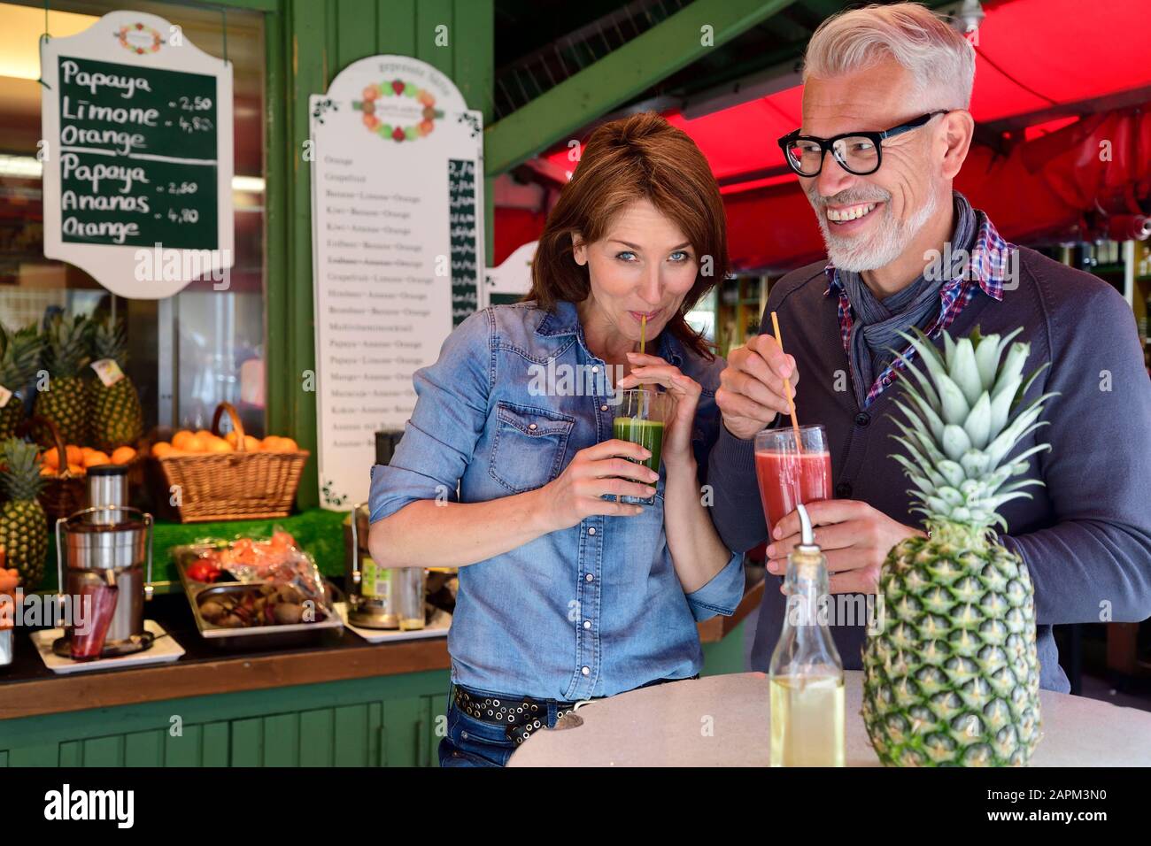 Portrait des glücklichen reifen Paares, das an einem Marktstand einen gesunden Saft trinkt Stockfoto