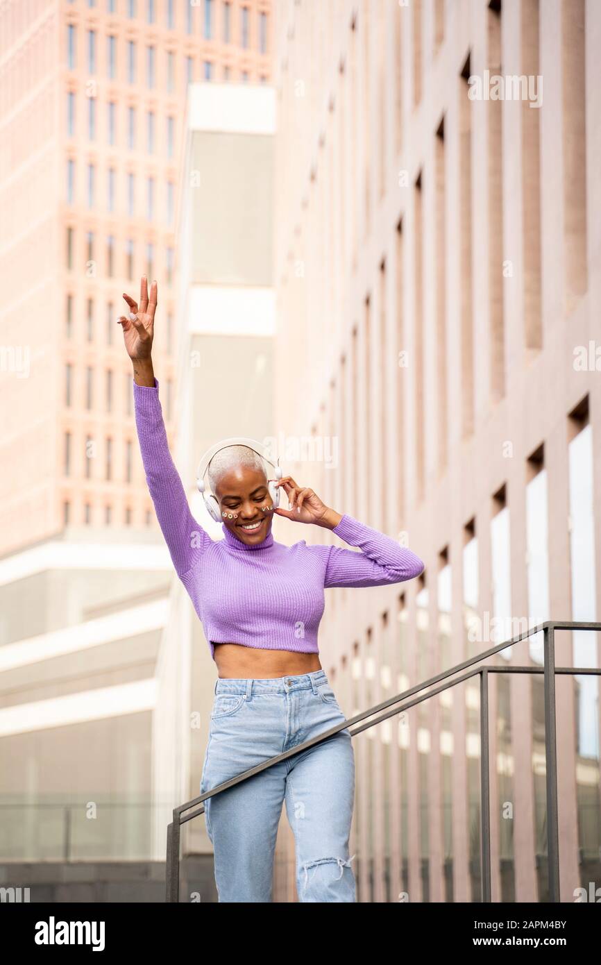 Porträt der weißen Frau mit weißen Kopfhörern, die Musik hören und in der Stadt tanzen Stockfoto