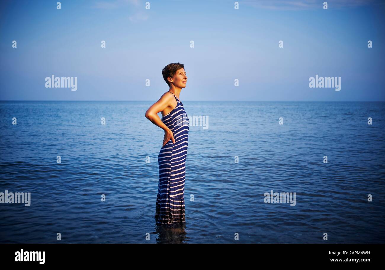 Frau, die im Meer steht und den Sonnenuntergang beobachtet, Italien Stockfoto