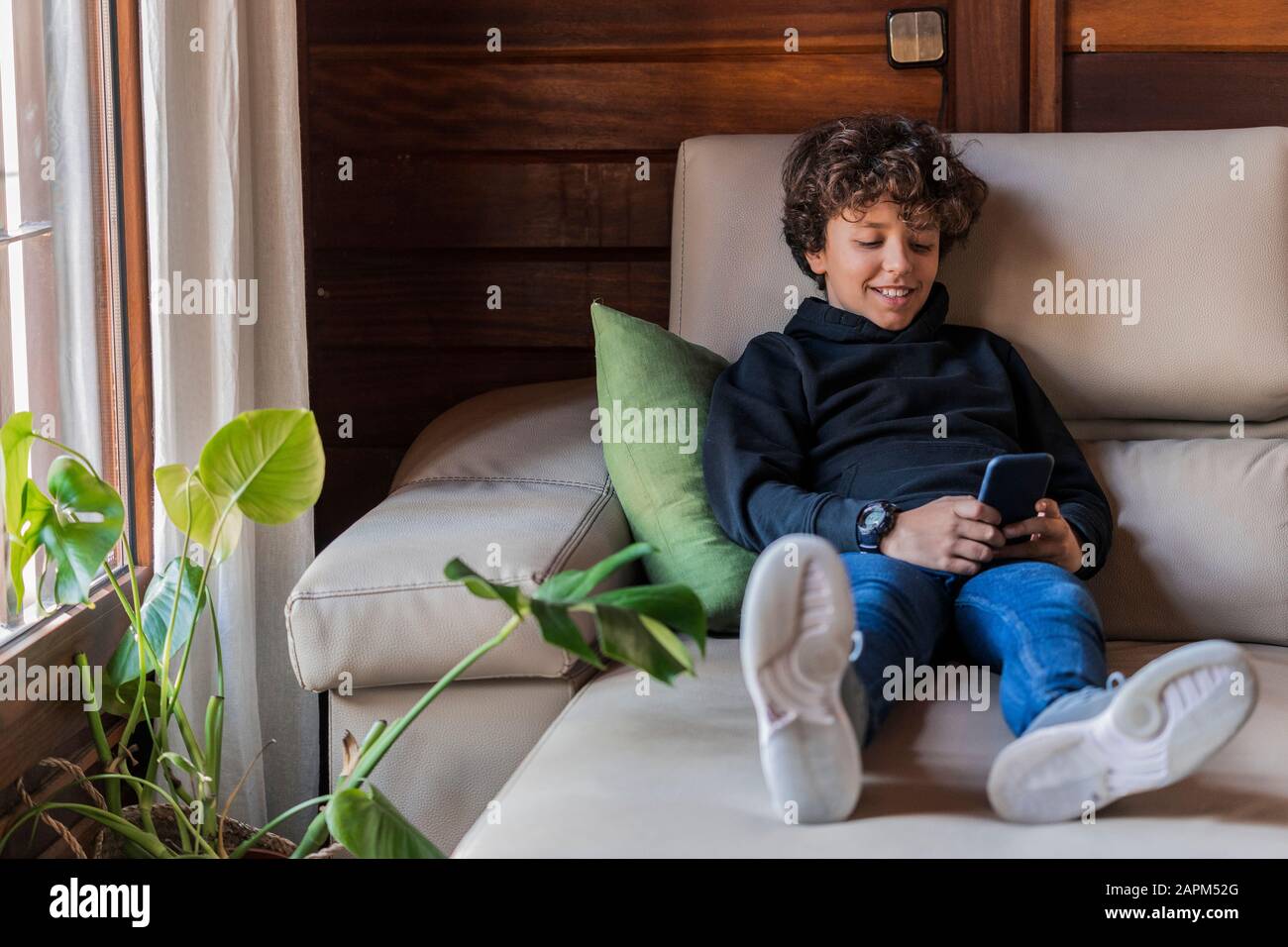 Lächelnder, entspannter Junge mit Handy auf der Couch zu Hause Stockfoto
