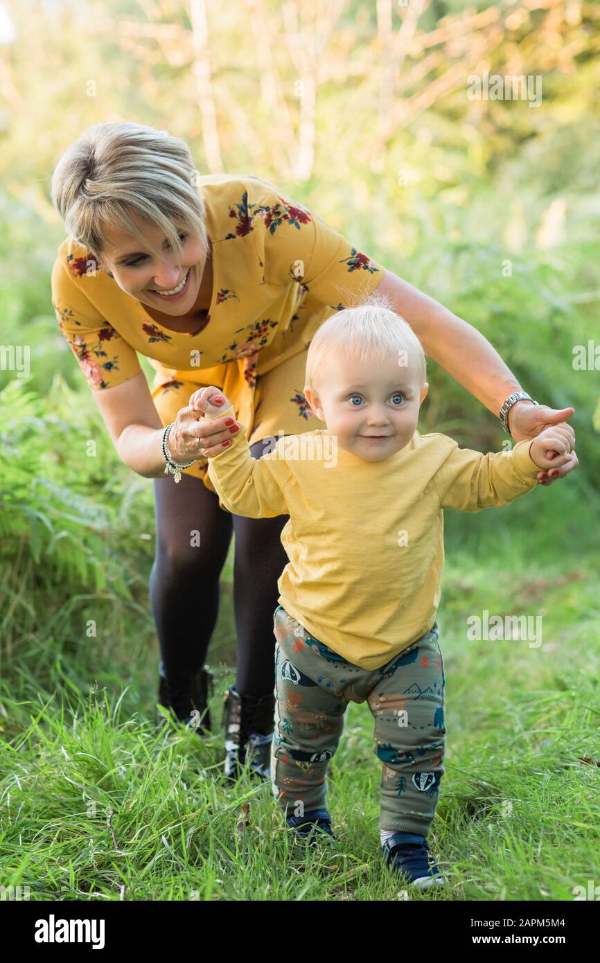 Mutter hilft dem kleinen Sohn, der auf einer Wiese spazieren geht Stockfoto