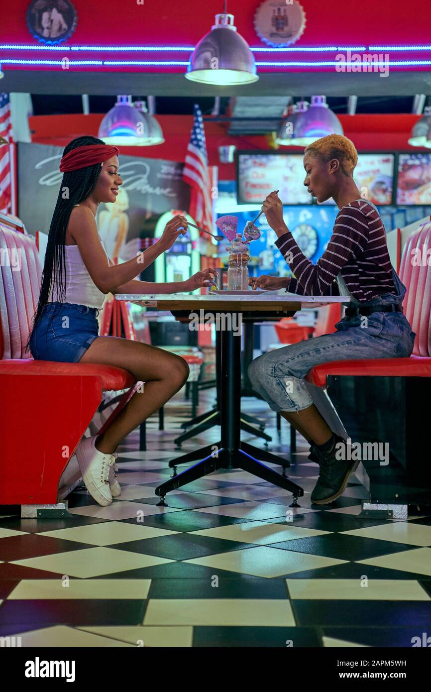 Zwei Frauen, die einen Milchshake auf dem Tisch eines amerikanischen Restaurants teilen Stockfoto
