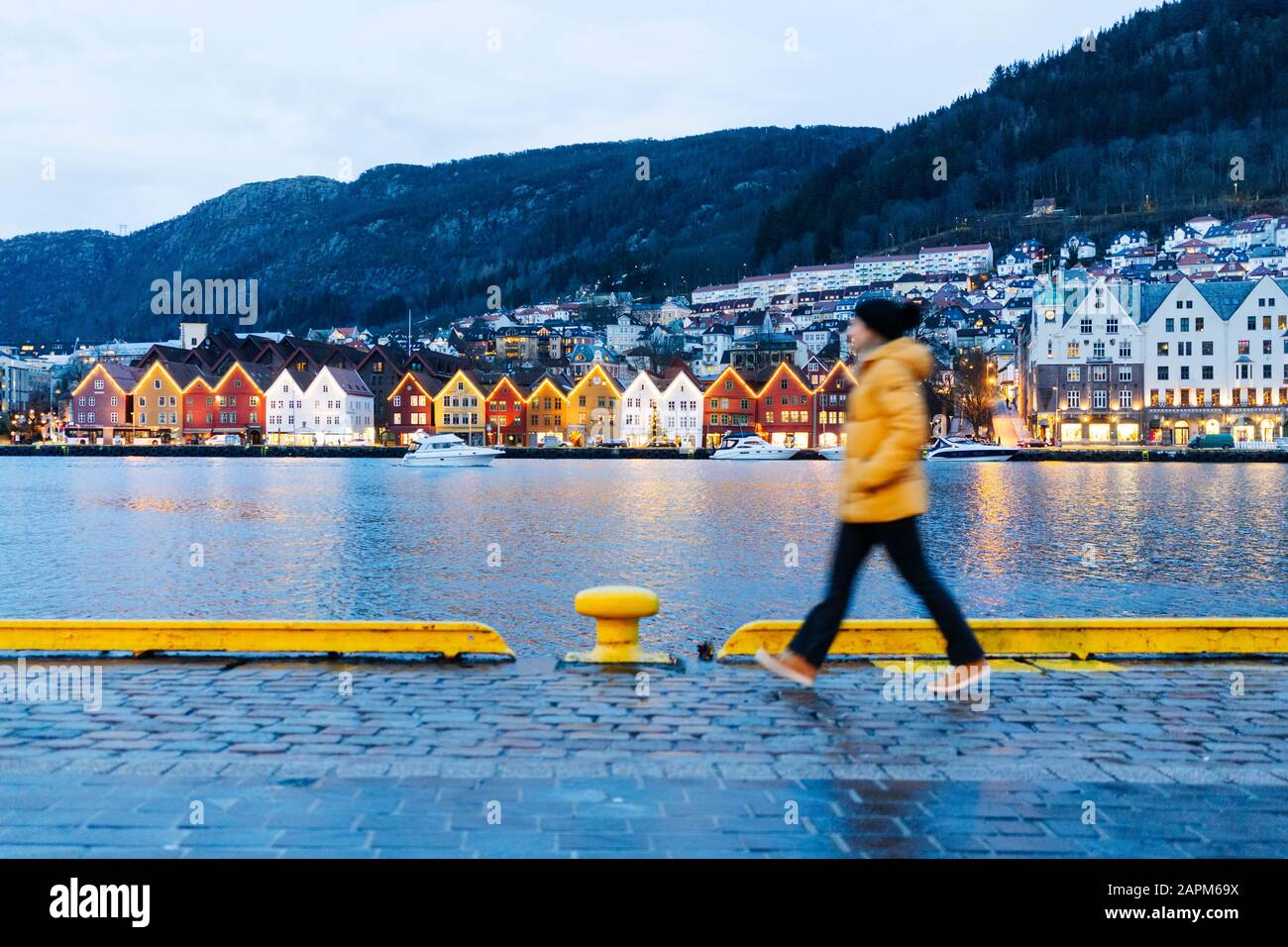 Frau, die eine gelbe Jacke trägt und am Hafen in Bergen, Norwegen spazieren geht Stockfoto