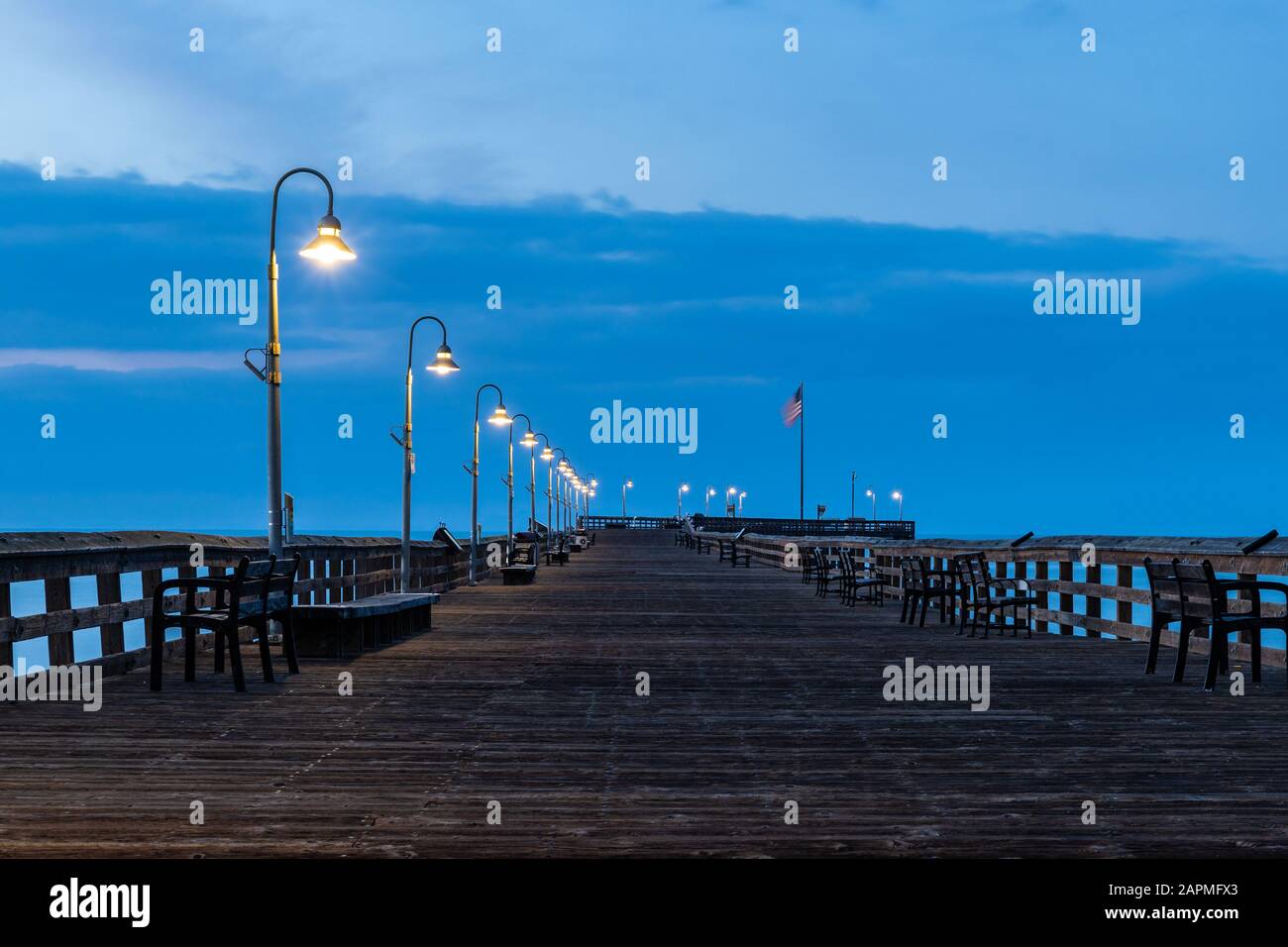 Ventura Pier, Blick auf den Seitenrand vor Sonnenaufgang. Gehweg verlassen; Lampen leuchten noch, blaue Wolken und Himmel im Hintergrund. Stockfoto