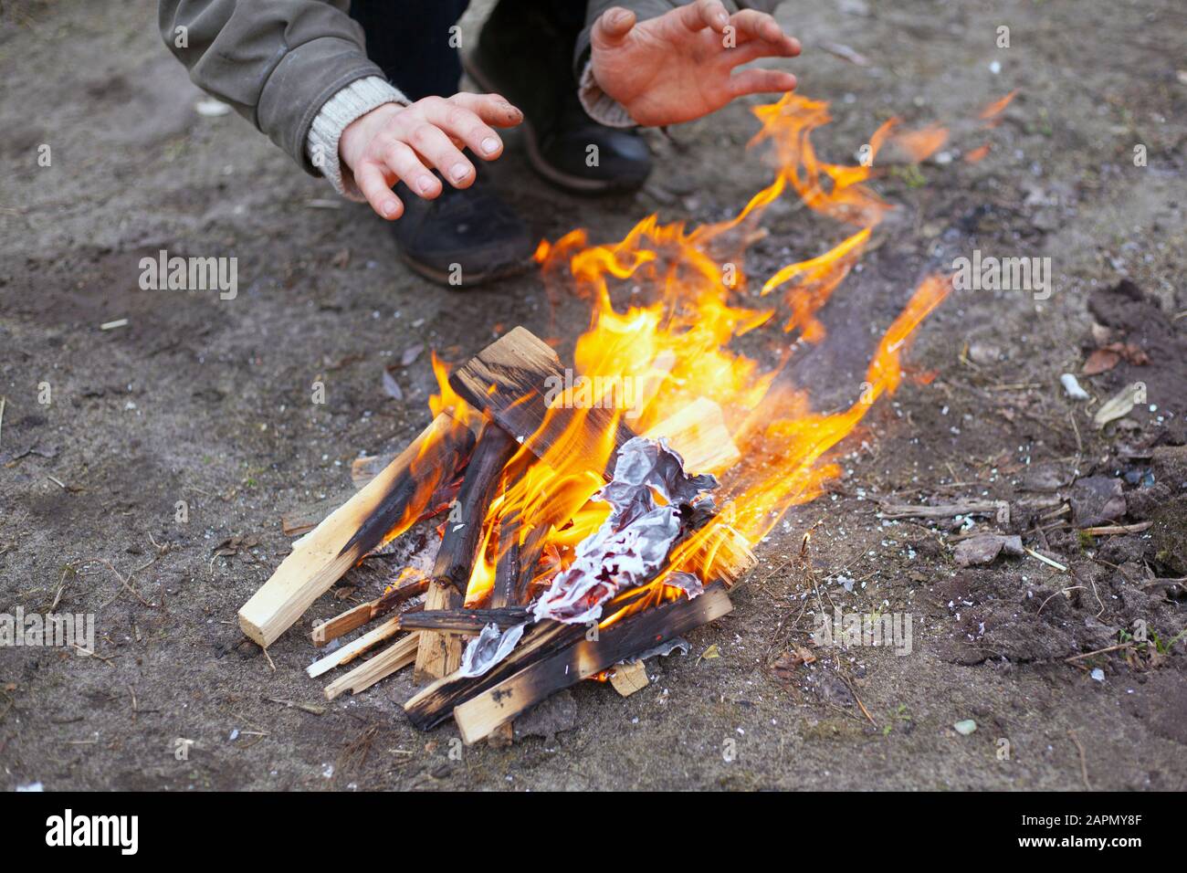Erwärmen Sie Ihre Hände am Feuer. Der Kerl versucht, die Kälte mit Flamme loszuwerden. Stockfoto