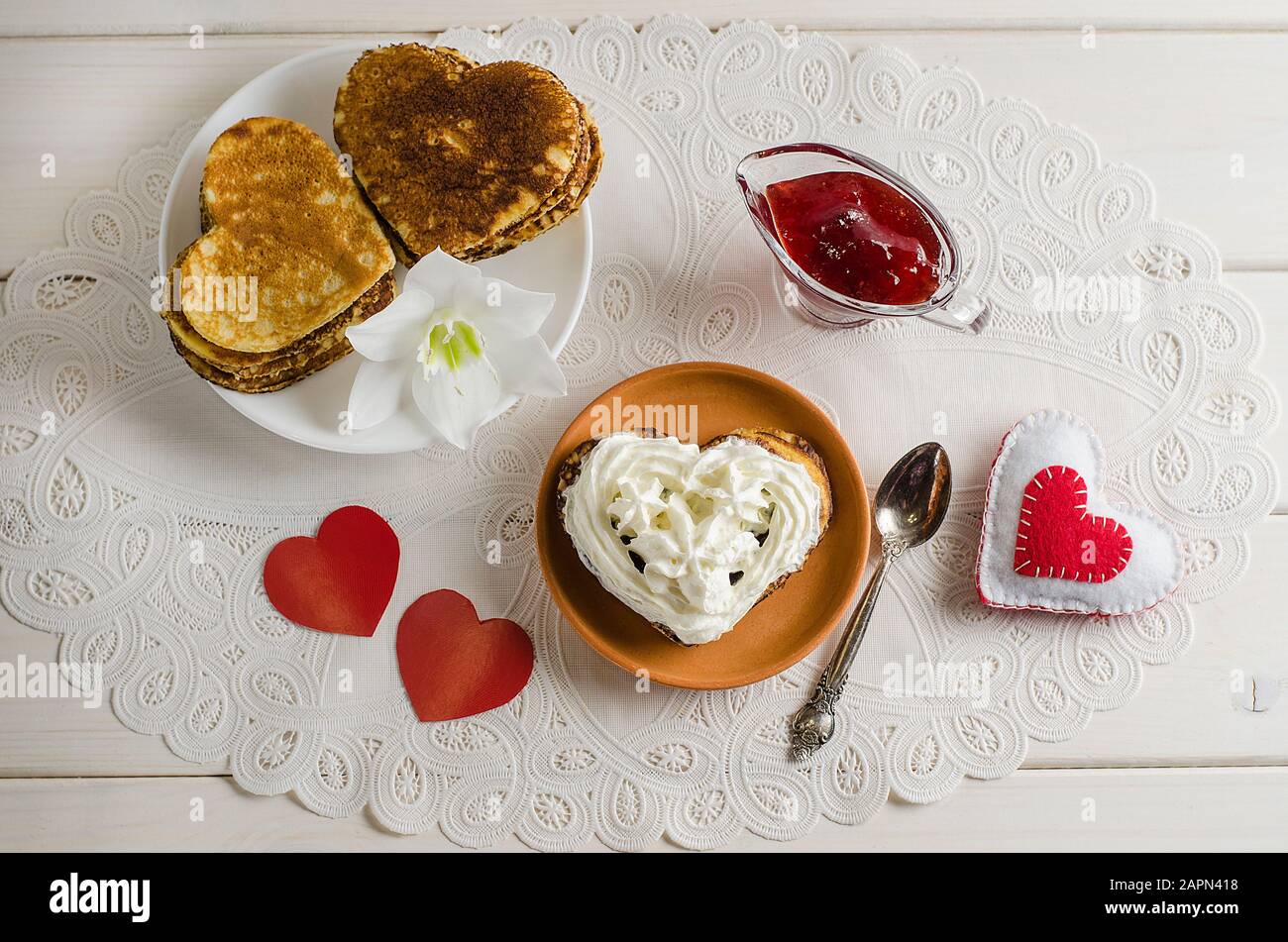 Brüter, Pfannkuchen in Form von Herzen mit Schlagsahne und Marmelade an einer weißen Spitzen-Serviette mit roten Herzen, romantisches Frühstück zum Valentinstag. Co Stockfoto