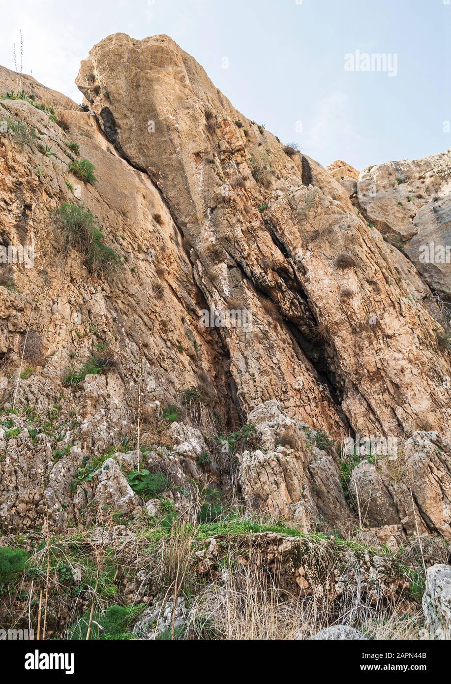 Geneigte Felsformation aus Kalkgestein in der Nähe eines prat in wadi qelt am Westufer mit Pflanzen in den Spalten und den Ruinen eines uralten Aquädukts im fo Stockfoto