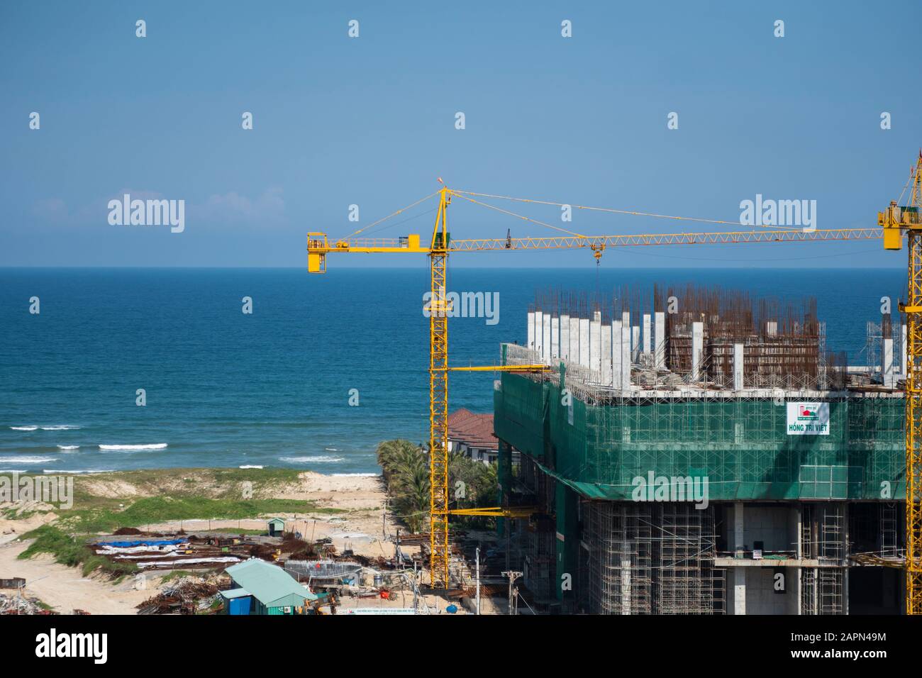 VIETNAM da NANG - April 10, 2019: Krane und Gebäude Baustelle gegen den blauen Himmel und das Meer. Metall Bau der unvollendete Gebäude auf Stockfoto