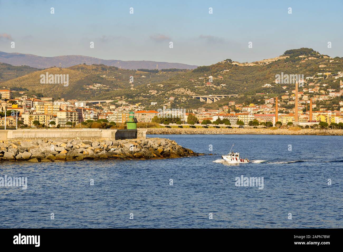 Malerische Aussicht auf die Küstenstadt Oneglia, Riviera der Blumen, mit einem Boot, das an einem sonnigen Tag vor dem grünen Leuchtturm, Imperia, Italien, vorbeiführt Stockfoto