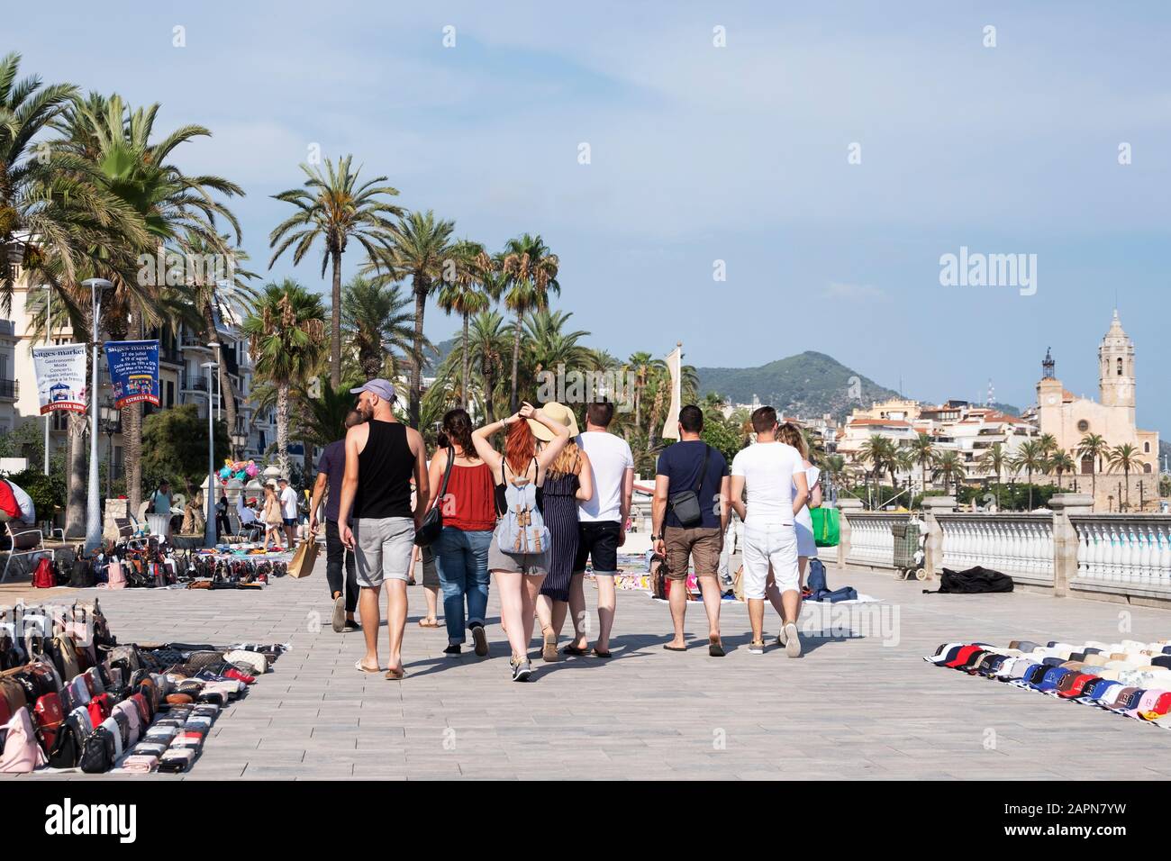 Sitges, SPANIEN - 27. JULI 2018: Menschen, die am beliebten Passeig de la Ribera Esplanade in Sitges, Spanien, spazieren und das Sant Bartomeu i Santa T hervorheben Stockfoto