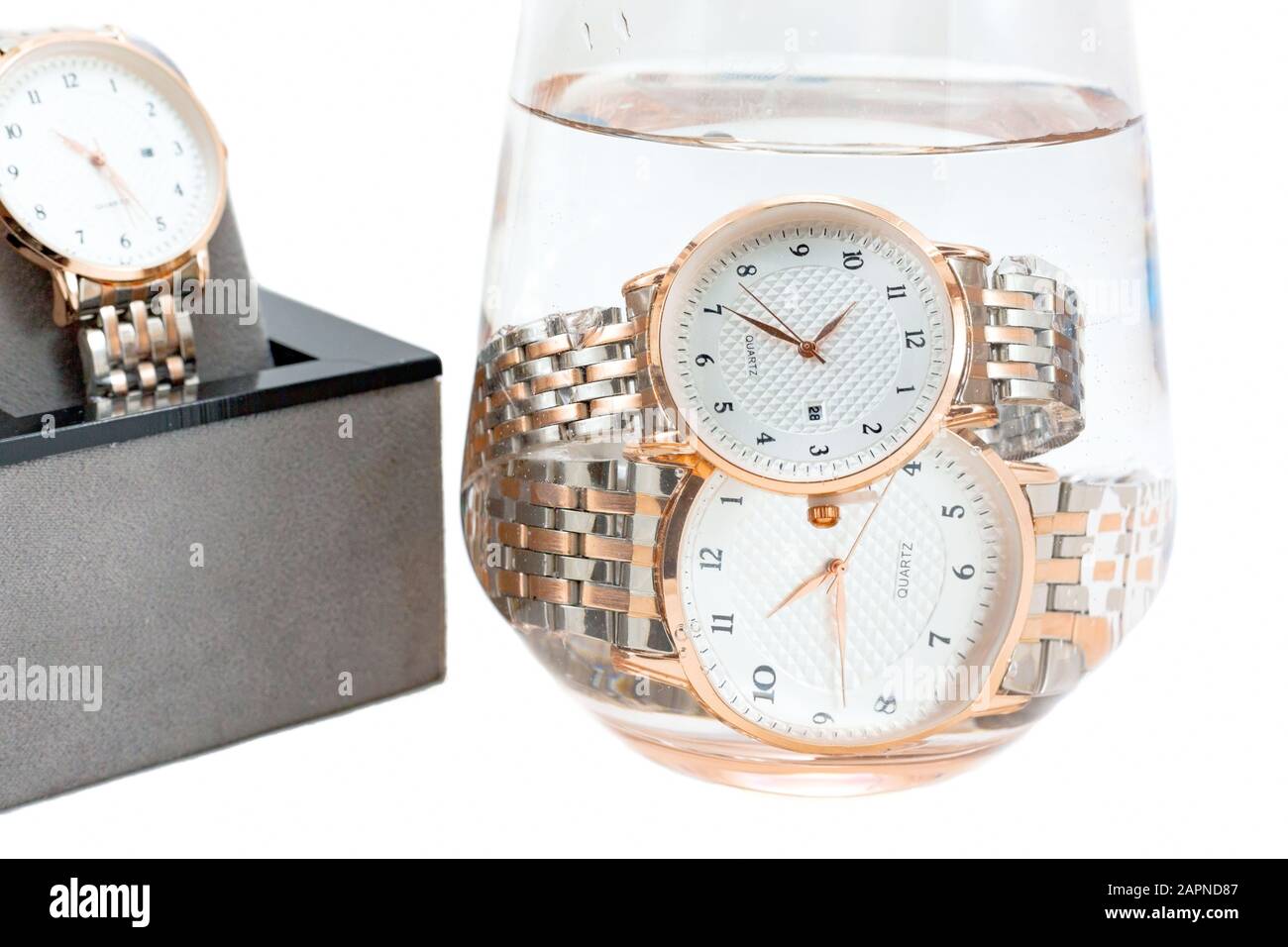 Klassische goldfarbene wasserdichte klassische Armbanduhren aus Metall tauchten in ein Glas Wasser und wurden in einem offenen Geschenkkasten präsentiert. Isoliert auf weißem Backgrot Stockfoto