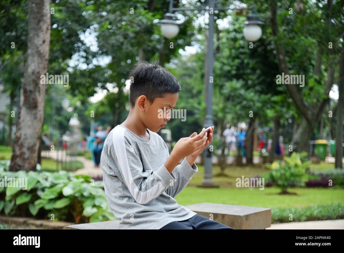 10 Jahre alt, Kid sitzt auf dem Stuhl im Park und spielt Online-Spiel, mit seinem Mobilgerät, Handtelefon Stockfoto