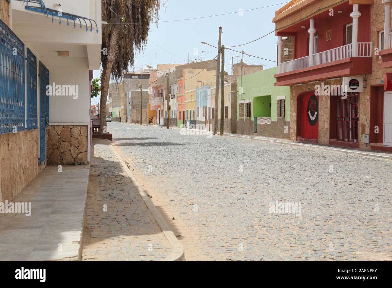 Eine einsame Hauptstraße zur Siesta Time mit bunten Geschäften und Häusern am Straßenrand in Santa Maria, Sal, Kap Verde, Afrika Stockfoto