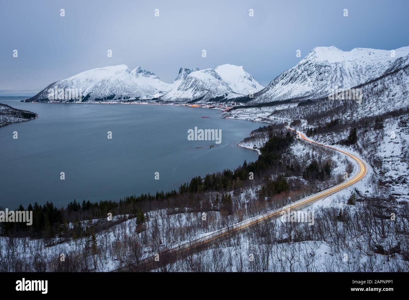 Blick über Senja am Winterabend mit Bergen und Fjord und Lichtwegen auf der Straße, Bergsbotn, Norwegen Stockfoto