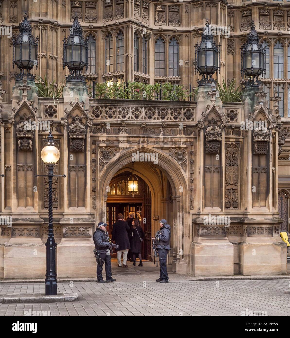 Bewaffnete Wachleute, die vor Den Häusern des Parlamentseingangs stehen, während Besucher (Rückansicht), Westminster, London UK, eindringen. Die Polizei bewacht die Regierung. Stockfoto