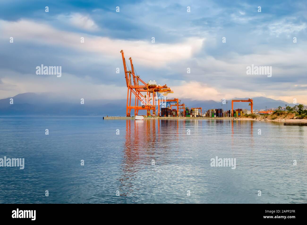 Leuchtend orangefarbene Ladekräne und gestapelte Frachtcontainer am Hafendock in Rijeka, Kroatien. Haupthafen im Osten der Stadt bei Sonnenuntergang mit schöner Aussicht Stockfoto