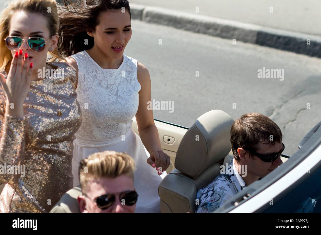 Junge Mädchen und Kerle fahren in schönen Outfits in einem Cabriolet, fröhliche Freunde fahren im Cabriolet-Auto. Offenes Auto. Sommer .Russland. Stockfoto