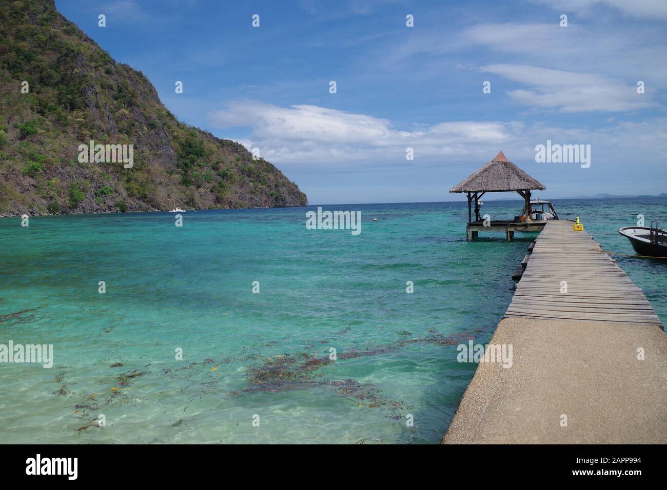 Ein Holzsteg, der in den Ozean ragt. Es gibt zwei Schnellboote und einen kleinen Schuppen am fernen Ende. Das Meer ist mit einem schönen Riff gefärbt. Stockfoto