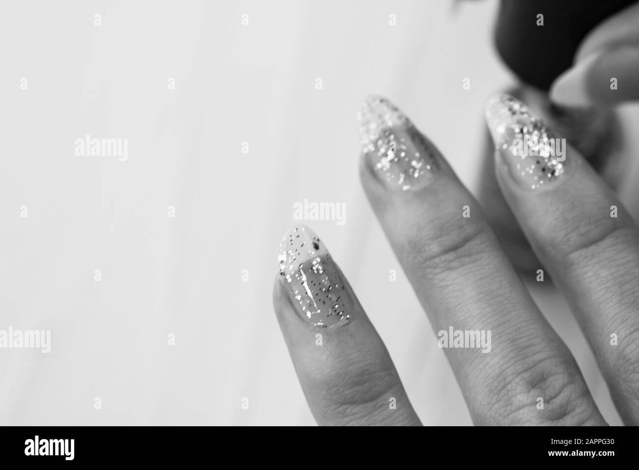 Weibliche Hände, die Maniküre machen, nagellack in goldener Glitzerfarbe auf weißem Hintergrund. Konzept des Haut- und Nagelpflegesalons Stockfoto