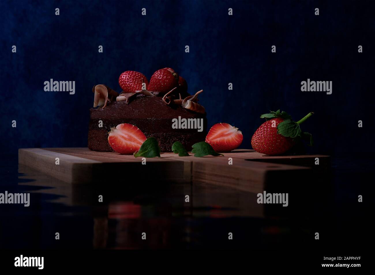Schokoladenkuchen mit Erdbeeren auf einem Holzbrett mit einer Spiegelung der Welligkeit des Wassereffekts Stockfoto