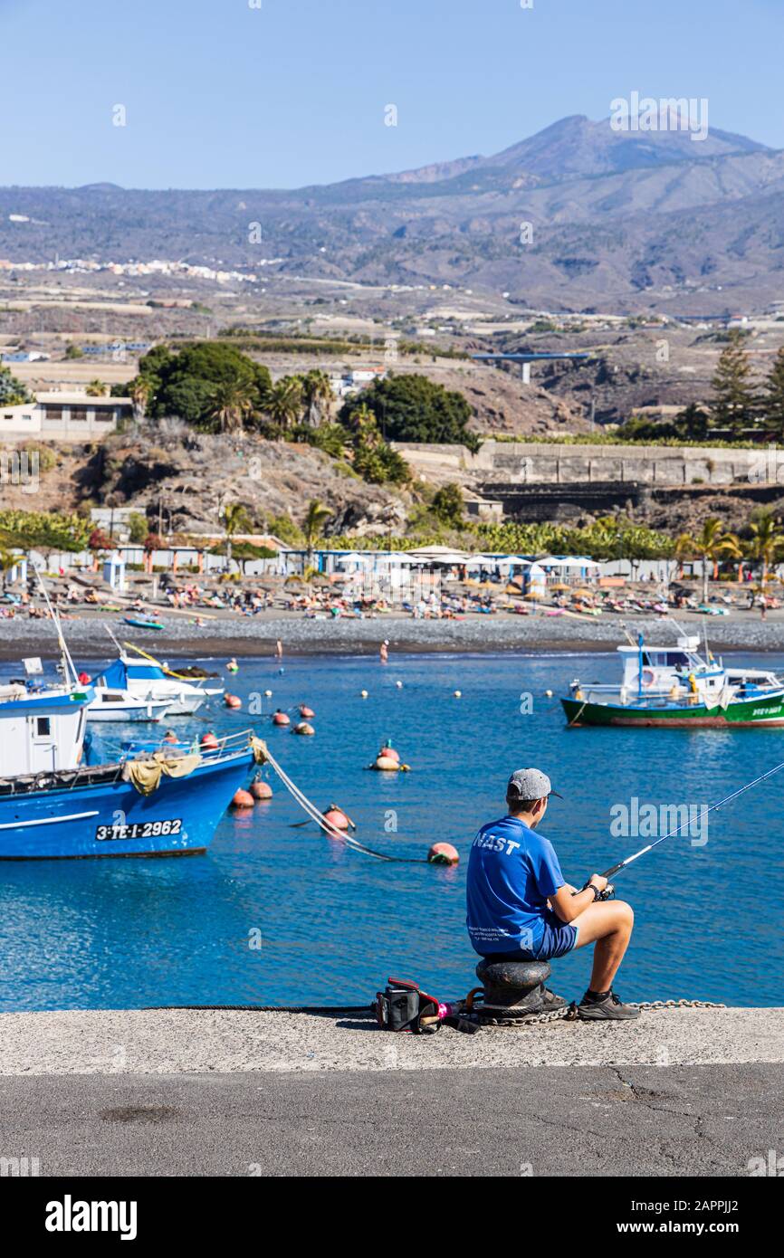 Angeln vom Kai im Hafen von Playa San Juan mit dem Berg teide, der hinter dem blauen Himmel zu sehen ist, auf Teneras, auf den Kanarischen Inseln, in Spanien Stockfoto