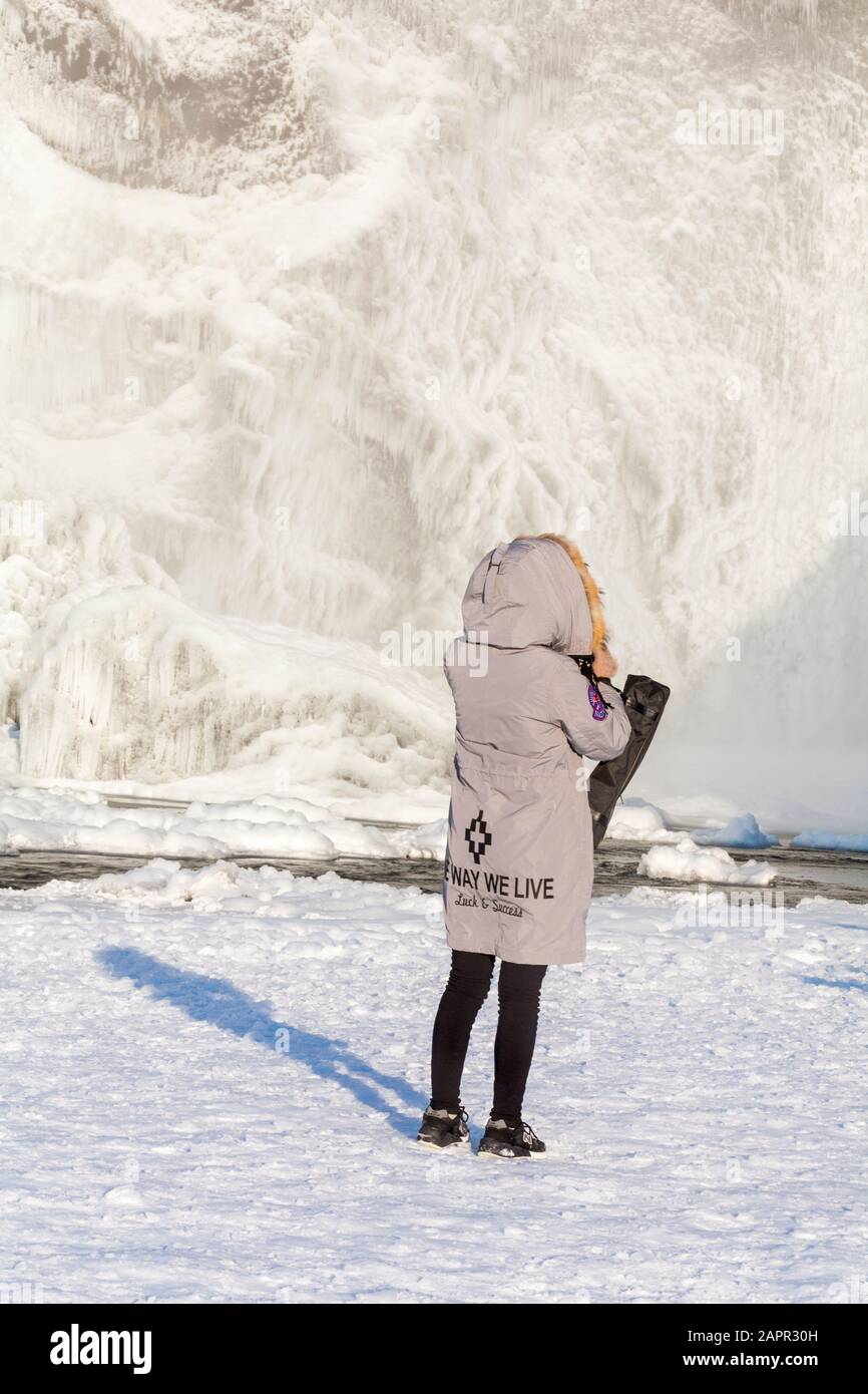 Besucher trägt die Art und Weise wir Leben Glück & Erfolg Mantel am Skogafoss Wasserfall, Island im Januar mit gefrorenen Eiszapfen Stockfoto