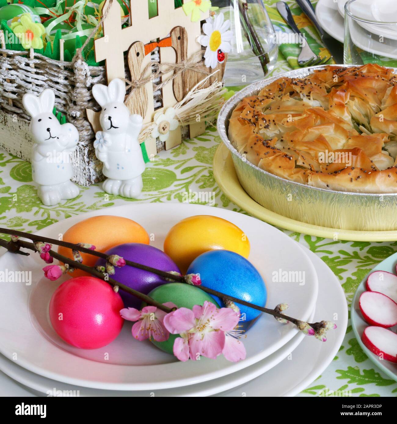 Konzept Frühlings-Feiertag.Ostertischdekoration. Eierkorb, Frühlingsblumen und bunte Einrichtung. Brot, Käse, Spinatkuchen, Fleischkugel, Gemüse. Stockfoto