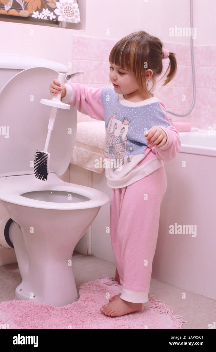 Kleines Mädchen im Schlafanzug, das mit oder mit einer toilettenbürste in einer toilette spielt Stockfoto