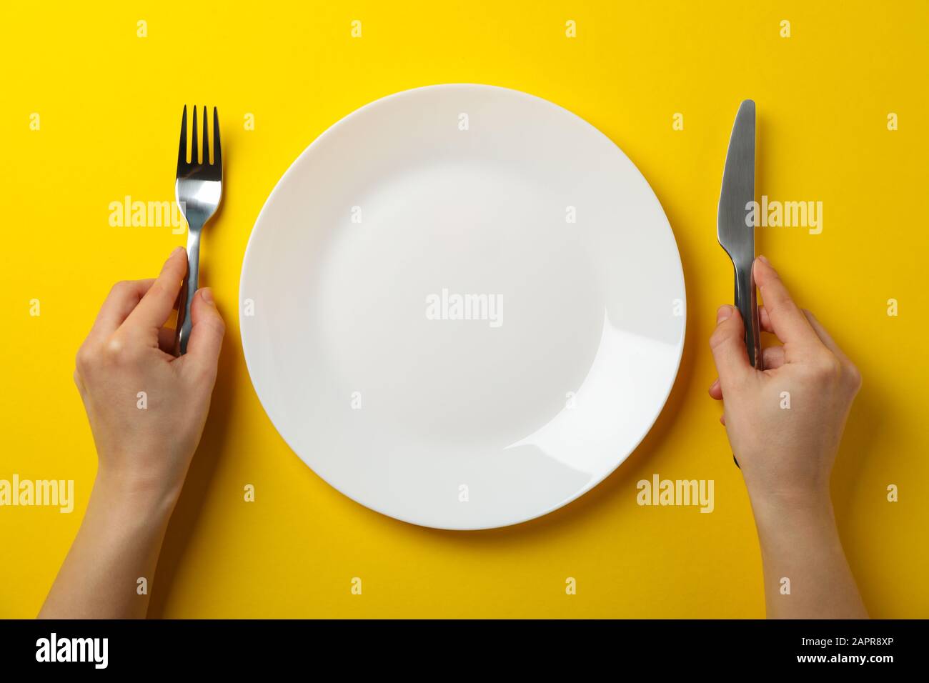 Weibliche Hände halten Gabel und Messer auf gelbem Hintergrund mit Platte, Draufsicht Stockfoto