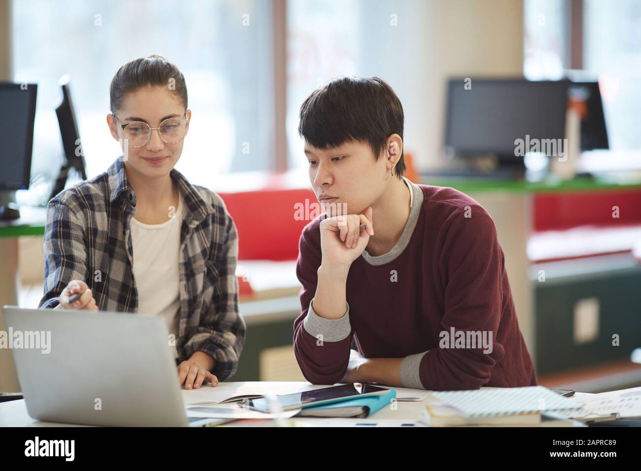 Junge Frau in legerer Kleidung, die auf den Laptop zeigt und dem jungen Mann nach dem Unterricht etwas neues Material erklärt Stockfoto