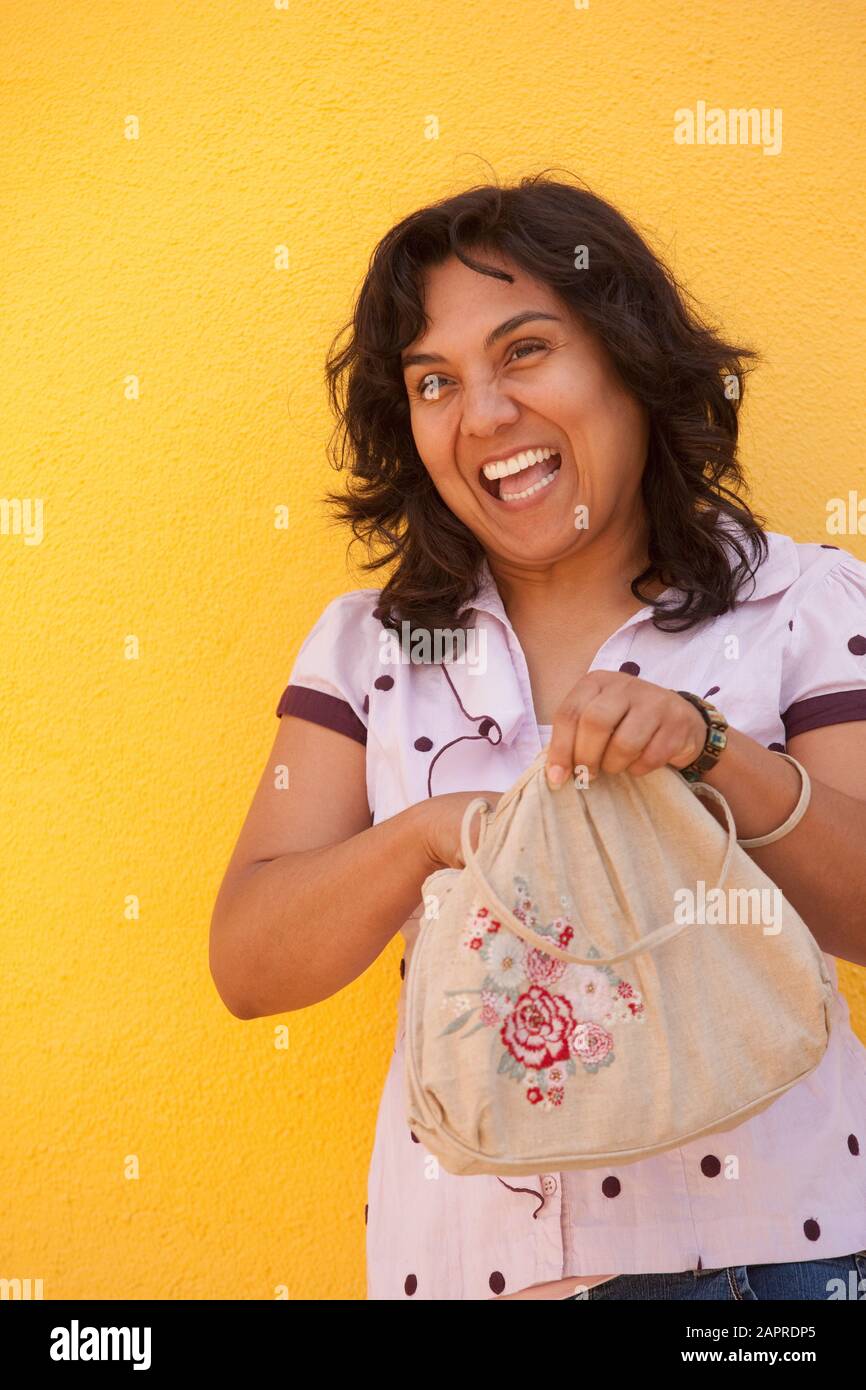 Porträt einer unbeschwerten Frau, die gegen ein helles Gelb steht Wand mit der Hand in der Handtasche Stockfoto