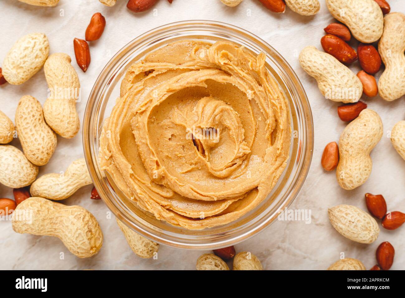 Cremige Erdnusspaste, Erdnussbutter in offenem Glasbecher im Zentrum von Erdnussnahrungshintergrund. Erdnüsse in der Schale, geschälte Erdnüsse auf weißem Hintergrund Stockfoto