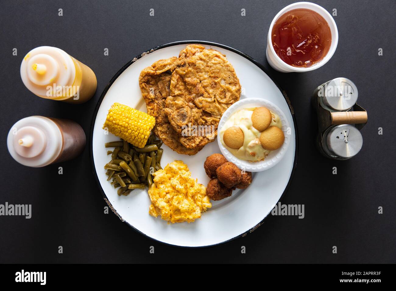 Schweinekotelteller mit Seiten und süßem Tee auf schwarzer Tischplatte Stockfoto