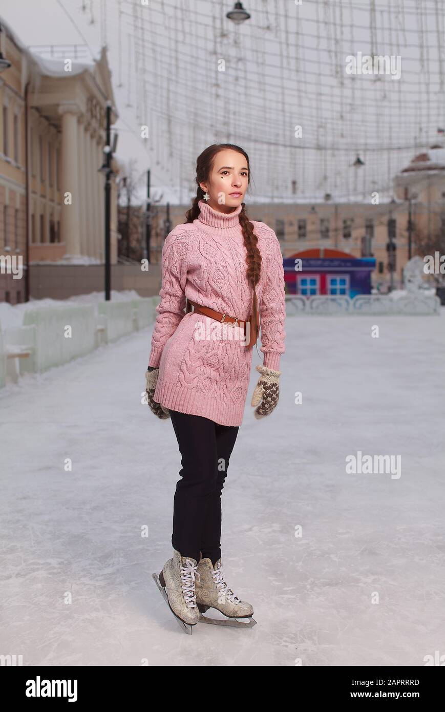 Junge hübsche Frau bekleidet rosafarbenes Sweatshirt, das in Schlittschuhbahnen, Eisbahn im Freien, auf Eis steht Stockfoto