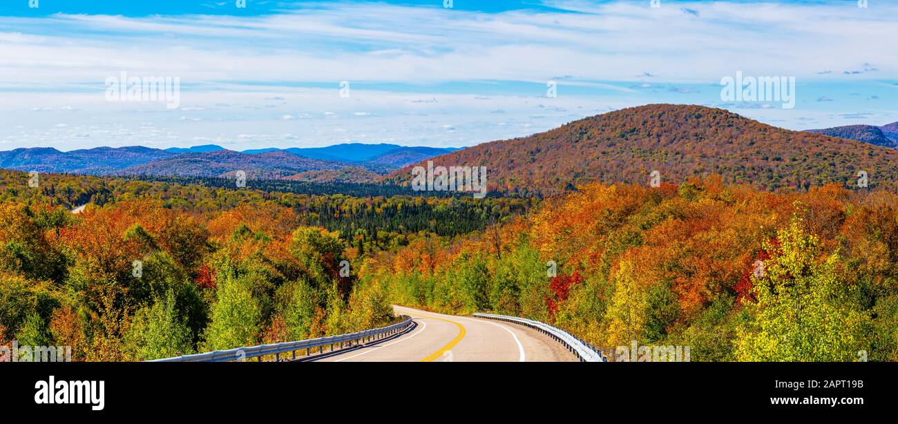 Herbstfarbenes Laub in einem Wald über den Hügeln und eine Straße, die durch sie in den Laurentian Mountains führt; Mont-Tremblant, Quebec, Kanada Stockfoto