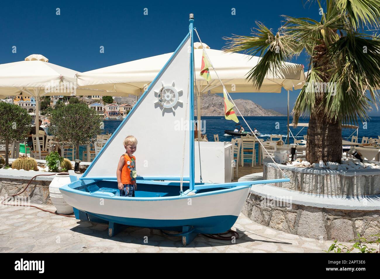 Drei Jahre alter Junge stehend in einem Boot vor einem Restaurant in Symi, Griechenland, Europa Stockfoto