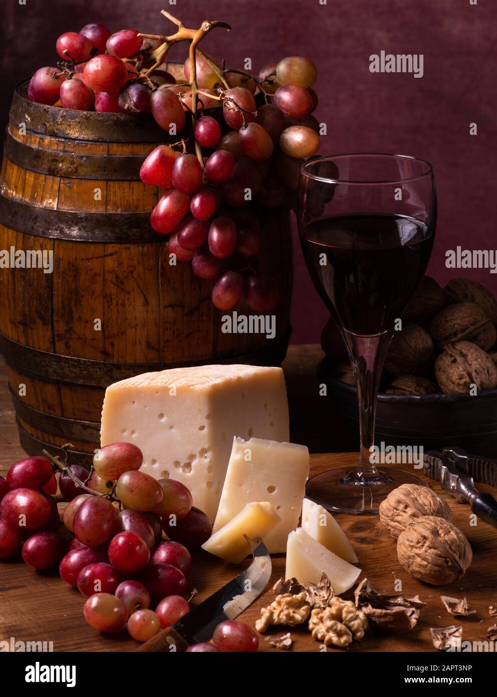 Auf alter Holzschneideplatte, gewürzter Ziegenkäse, Walnüsse, Trauben und Rotwein. Stillleben Stockfoto